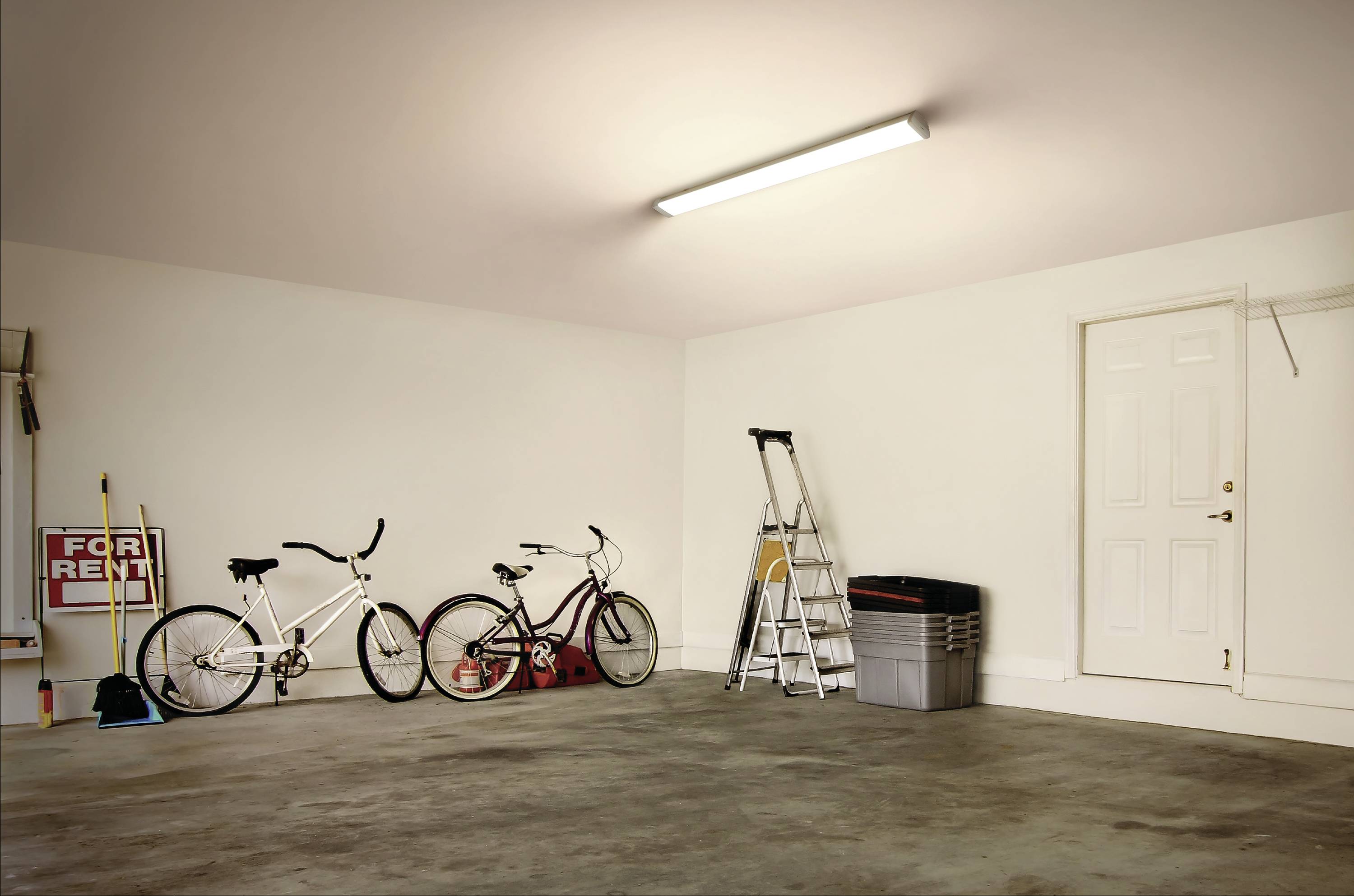 Eine leere Garage mit zwei Fahrrädern, einer Leiter und einem 'For Rent'-Schild an der Wand.