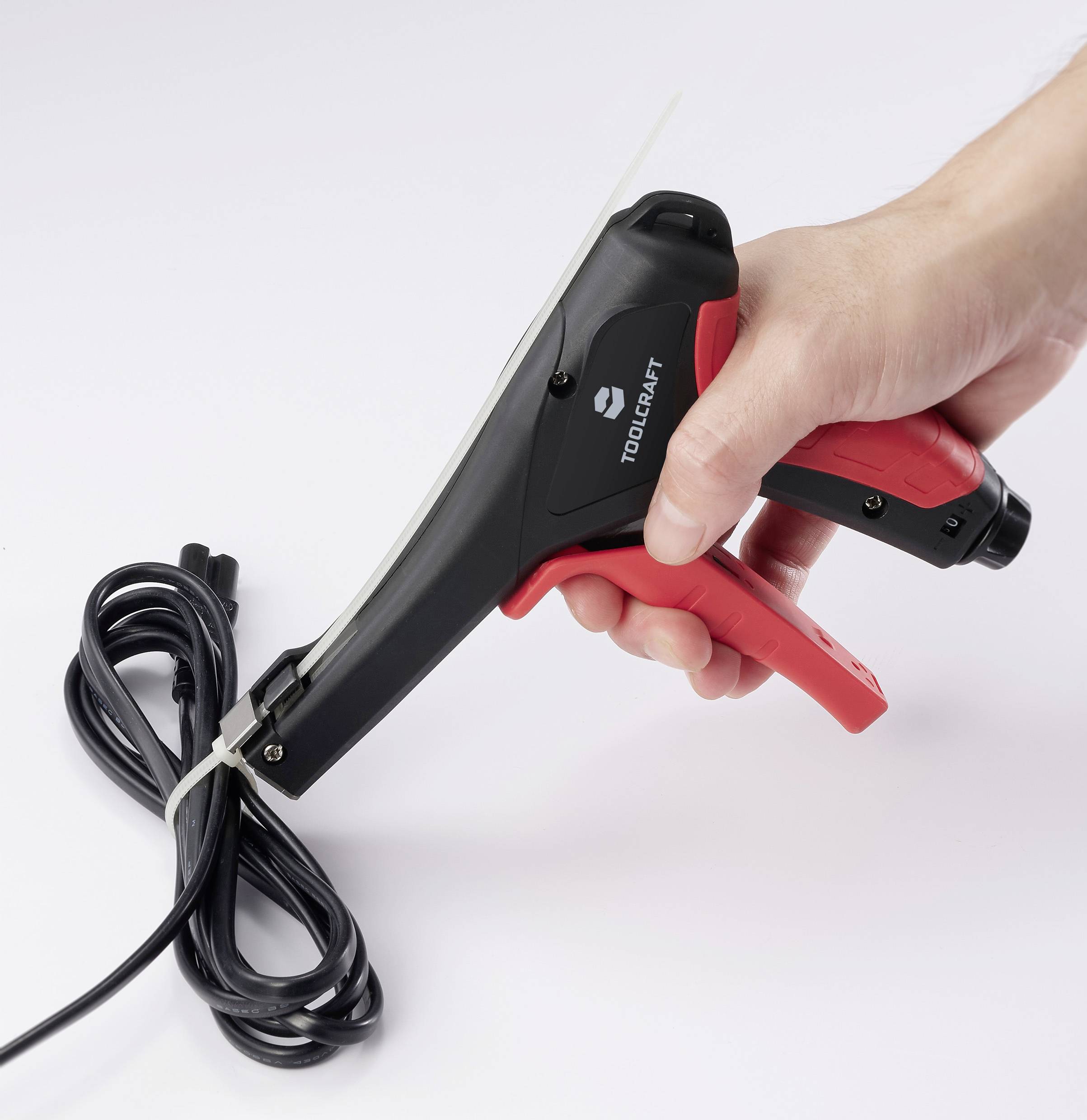 Eine Hand hält ein Kabel mit einer Zange, die einen Kabelbinder um das Kabel zieht. Das Werkzeug ist schwarz-rot.