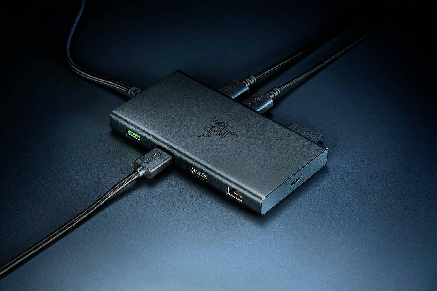 Ein schwarzer USB-Hub mit mehreren angeschlossenen Kabeln. Er liegt auf einer dunklen Oberfläche. Das Logo einer Marke ist sichtbar.