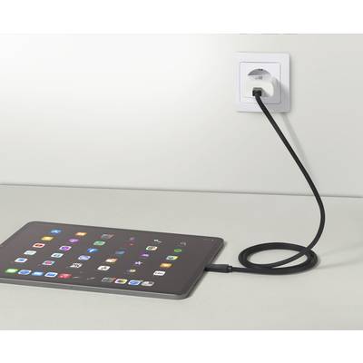Ein Tablet liegt auf einem Tisch und wird über ein schwarzes Kabel mit einer Wandsteckdose aufgeladen. Der Bildschirm zeigt verschiedene App-Symbole.