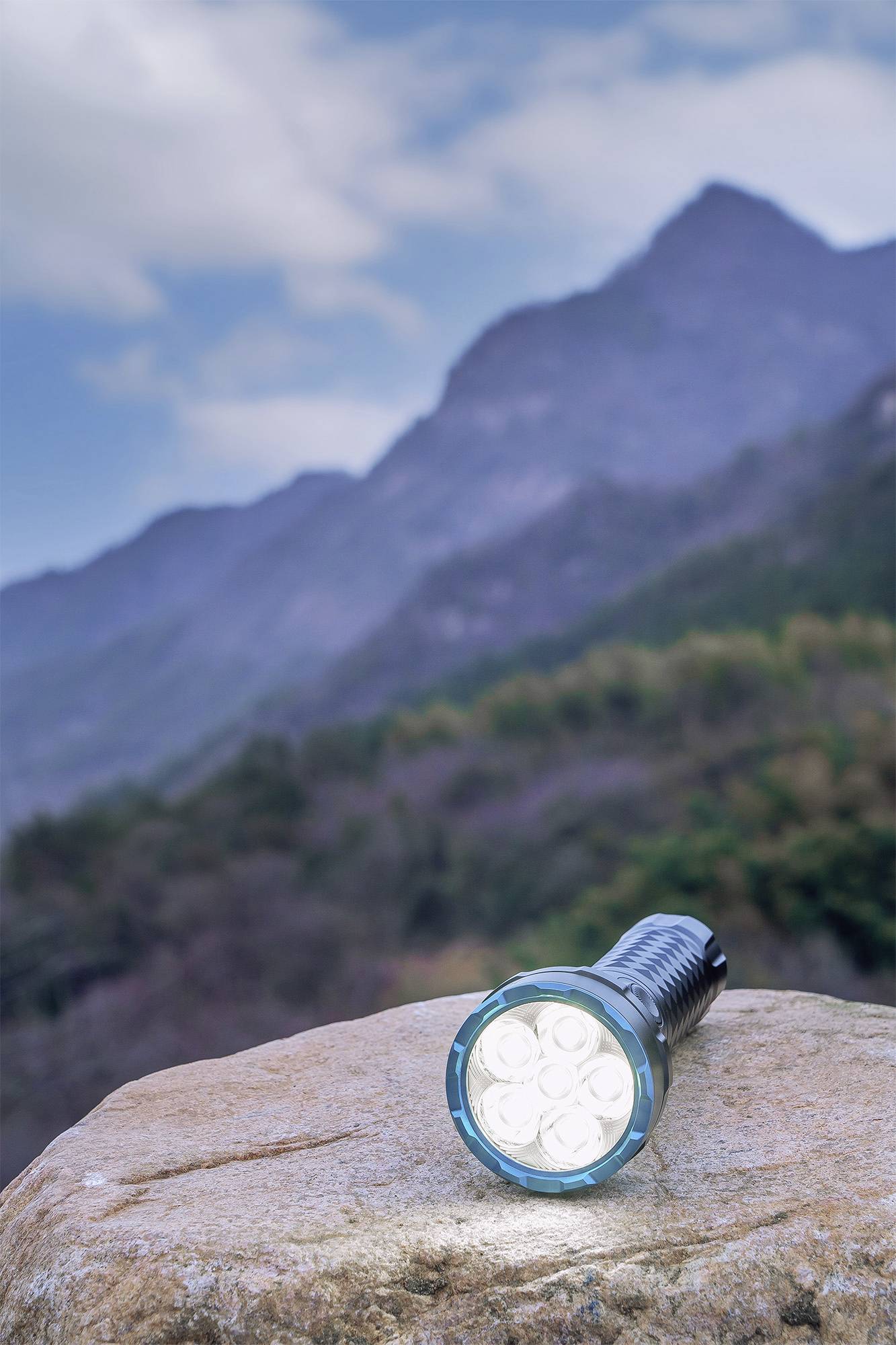 Taschenlampe leuchtet auf einem Felsen vor einer Berglandschaft mit bewölktem Himmel.