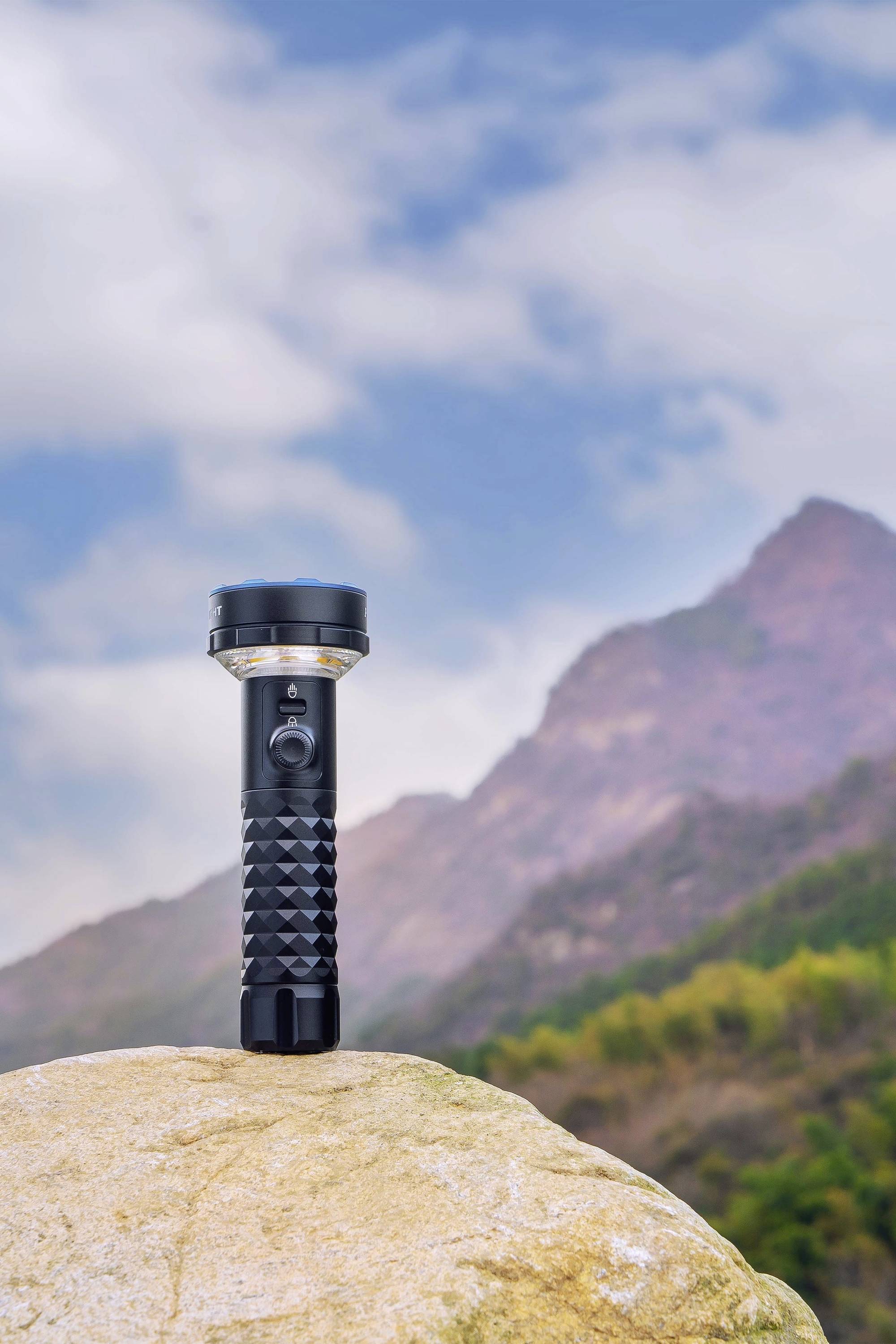Taschenlampe steht auf einem Felsen mit Berg und blauem Himmel im Hintergrund.