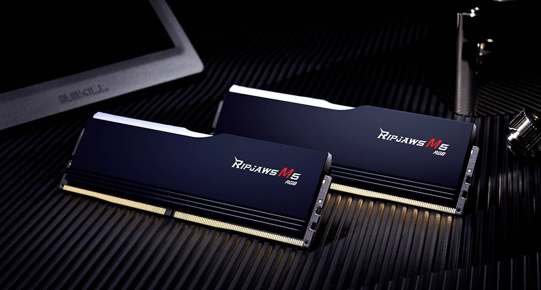 Zwei RAM-Module mit der Aufschrift 'Ripjaws M5' liegen schräg auf einer dunklen, strukturierten Oberfläche. Im Hintergrund ist teilweise ein Bildschirm sichtbar.