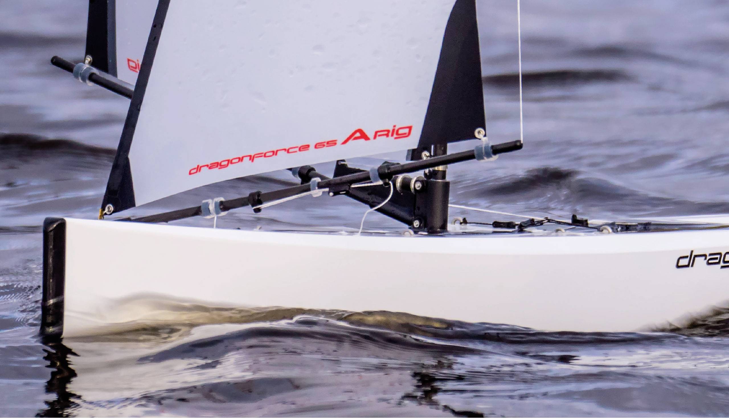 Ein Segelboot auf dem Wasser, fokussiert auf den Bug und das Segel. Der Markenname 'dragonforce 65' ist auf dem Segel sichtbar.