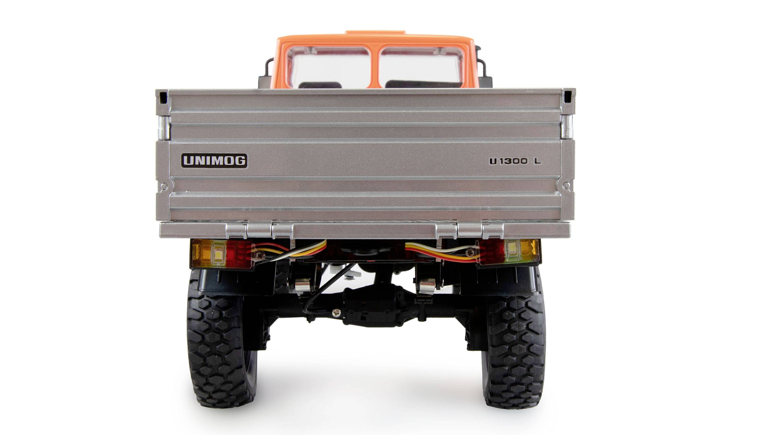 Ein Modell-Lkw vom Typ Unimog U1300L in orangefarbener und silberner Lackierung, aufgenommen von hinten, zeigt Details der Hinterräder und Ladefläche.