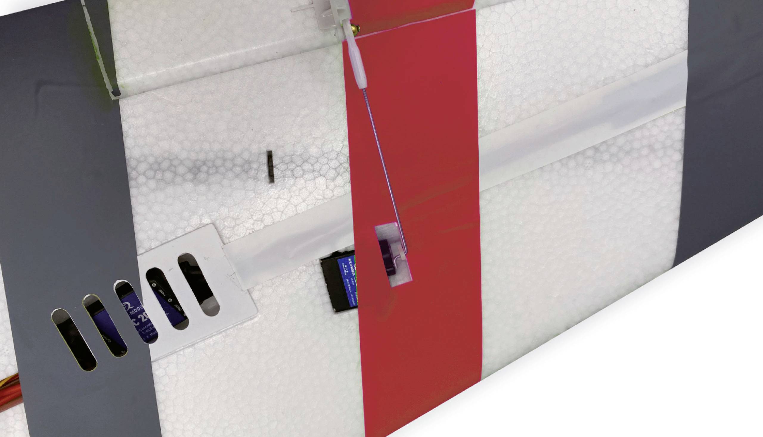 Nahaufnahme eines Modellflugzeugflügels mit rotem und grauem Muster auf einer weißen, schaumartigen Oberfläche.