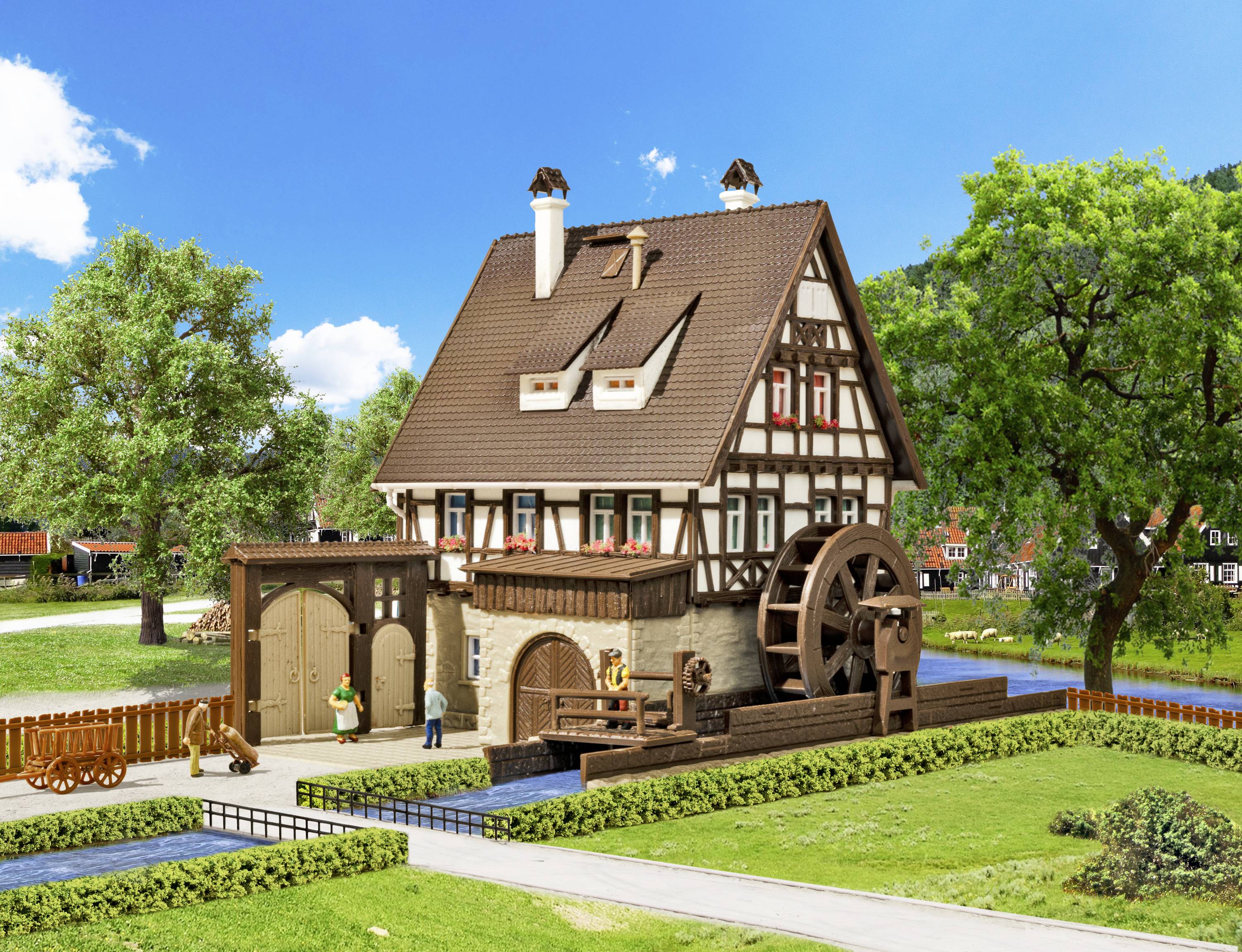 Fachwerkhaus mit Wasserrad und Figuren im Garten vor blauem Himmel; ländliche Szene mit Bäumen und Rasen.