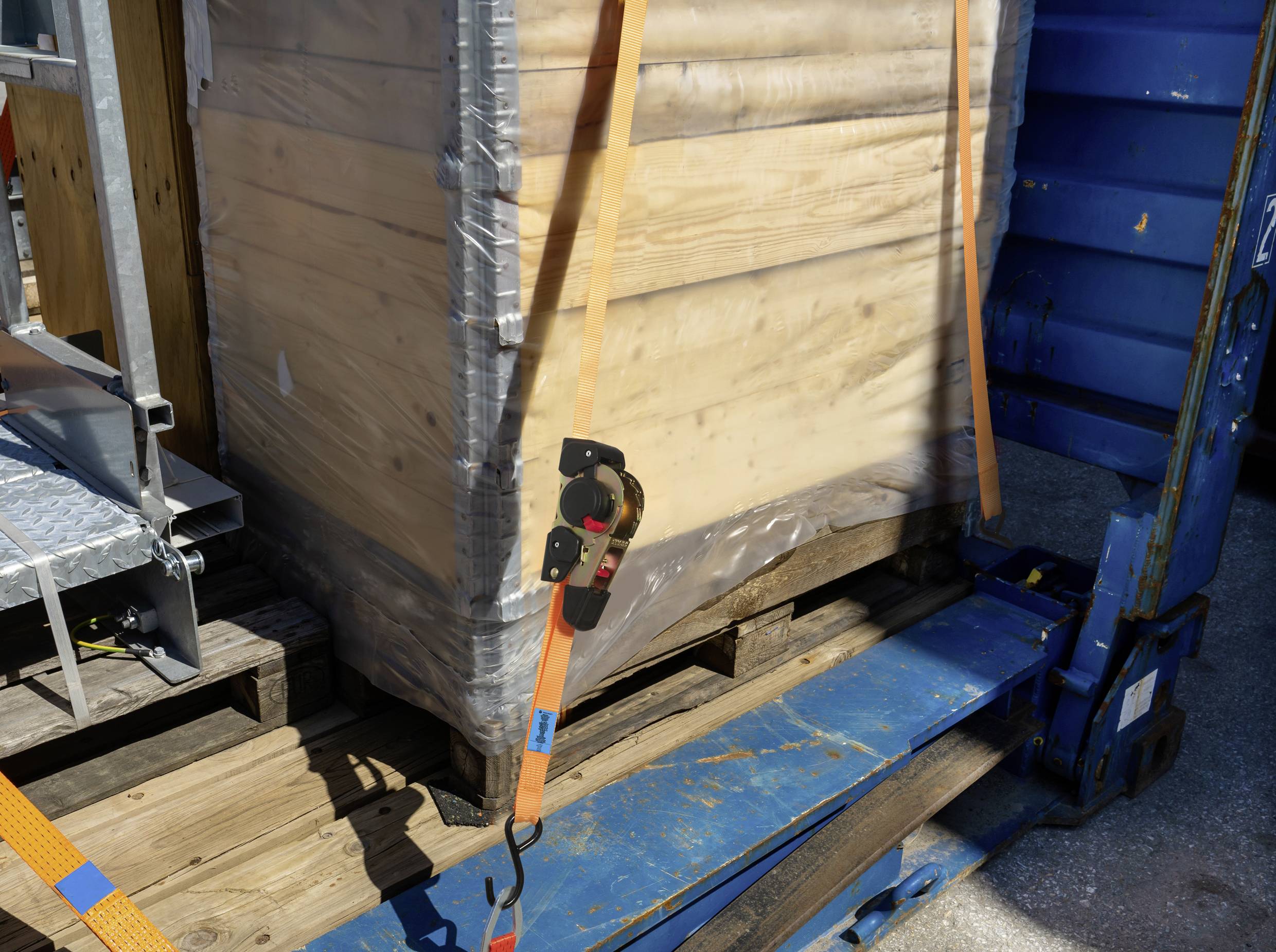 Eine Holzpalette wird mit Spanngurten auf einen LKW geladen. Die Gurte sichern die Ladung für den Transport.