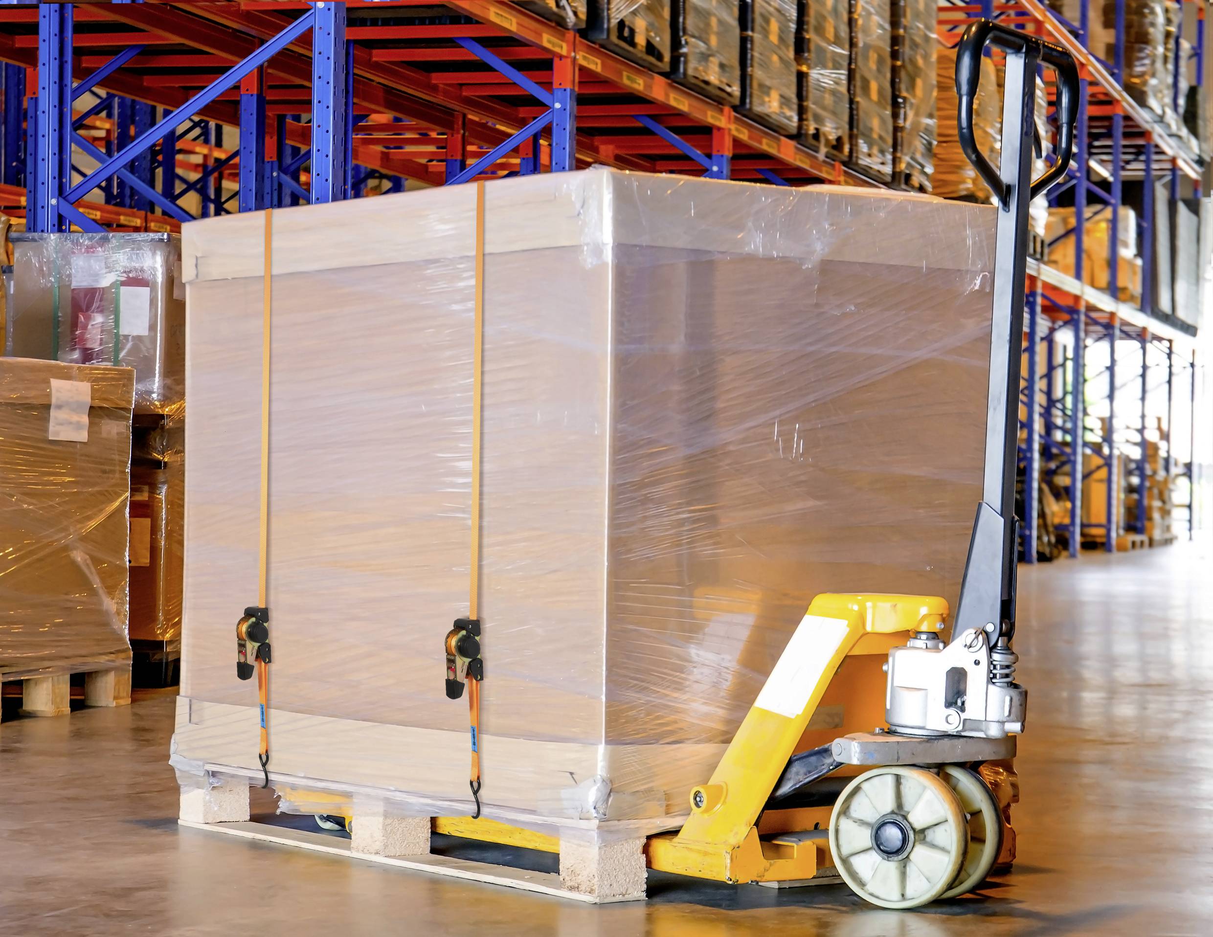 Ein großer, in Plastik eingewickelter Karton auf einer Palette wird in einem Lager mit einem Hubwagen transportiert.