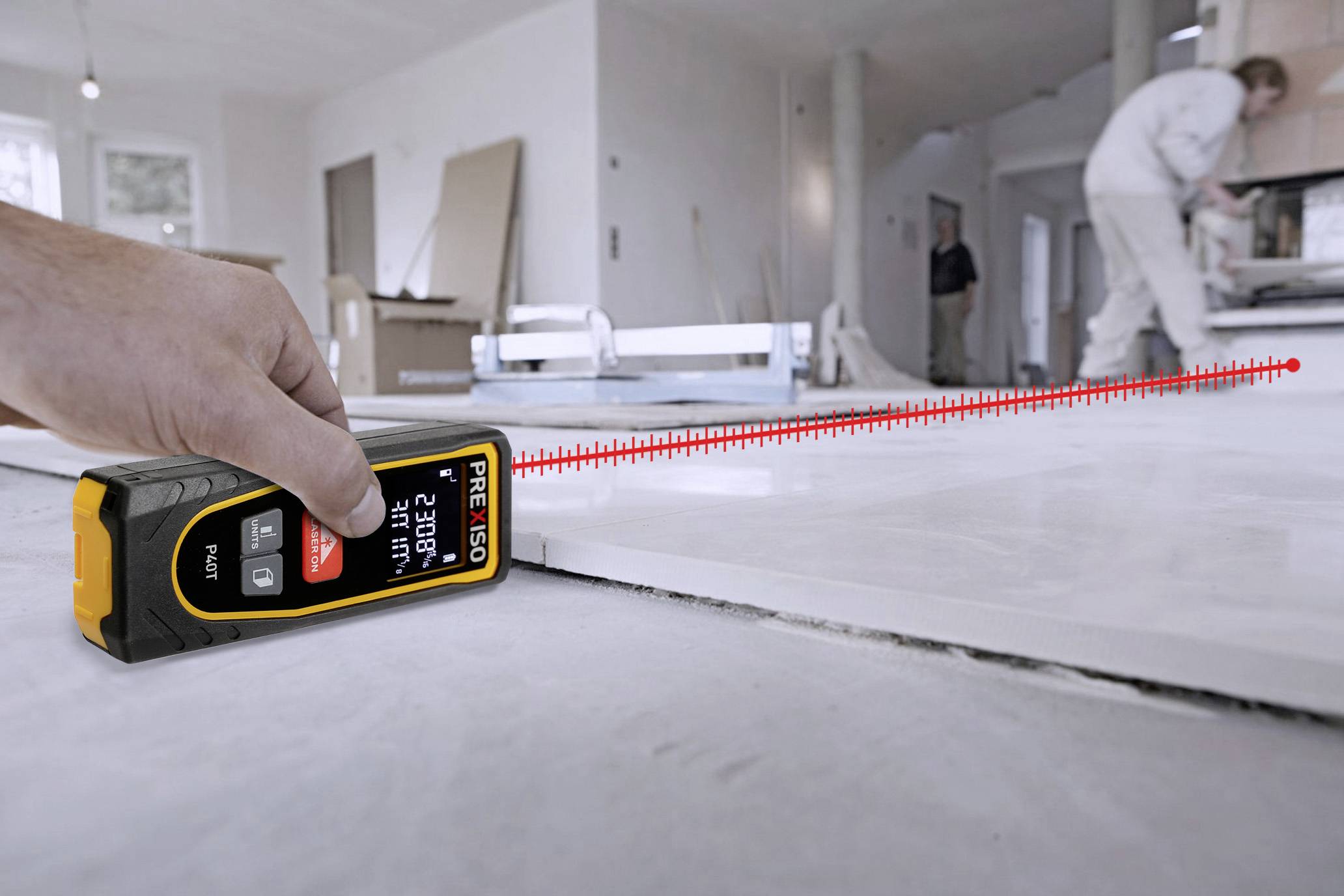 Eine Hand benutzt ein Laser-Entfernungsmesser, um den Abstand in einem Raum zu messen, während im Hintergrund Bauarbeiten stattfinden.