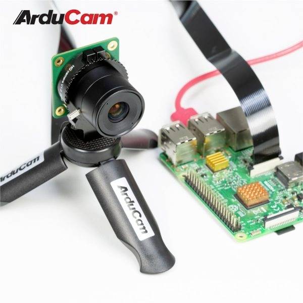 'ArduCam'-Kamera auf Stativ neben einer Raspberry Pi-Platine mit verbundenem Flachbandkabel, vor weißem Hintergrund.