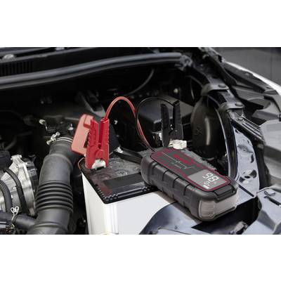 Eine tragbare Autobatterie-Starthilfe, angeschlossen an eine Autobatterie unter einer geöffneten Motorhaube, bereit zum Starten.