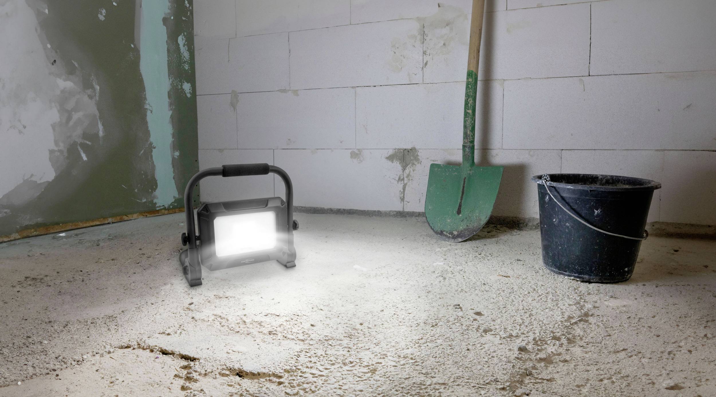 Eine Baustelle mit einem Eimer, einer Schaufel und einer leuchtenden Arbeitsleuchte auf einem Betonboden.