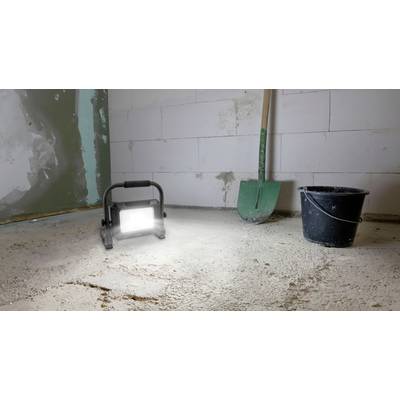 Eine Baustelle mit einem Eimer, einer Schaufel und einer leuchtenden Arbeitsleuchte auf einem Betonboden.