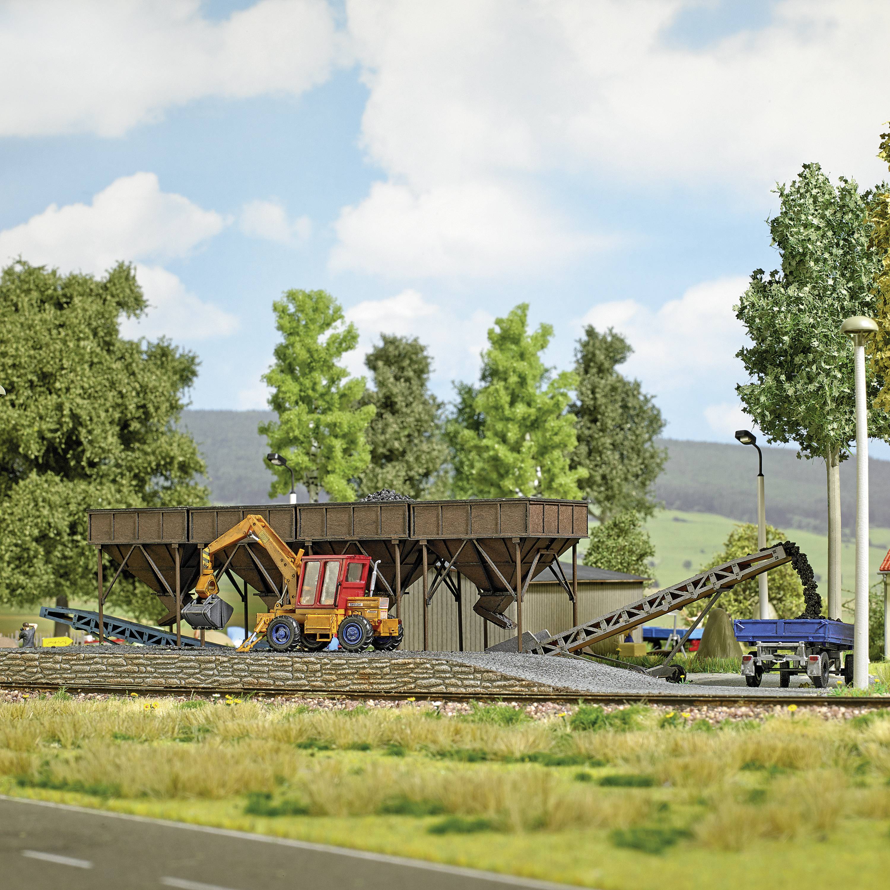 Ein Miniatur-Modelldorf zeigt eine Baustelle mit einem Kran, einem Traktor und einem Förderband, umgeben von Bäumen und Wiesen.