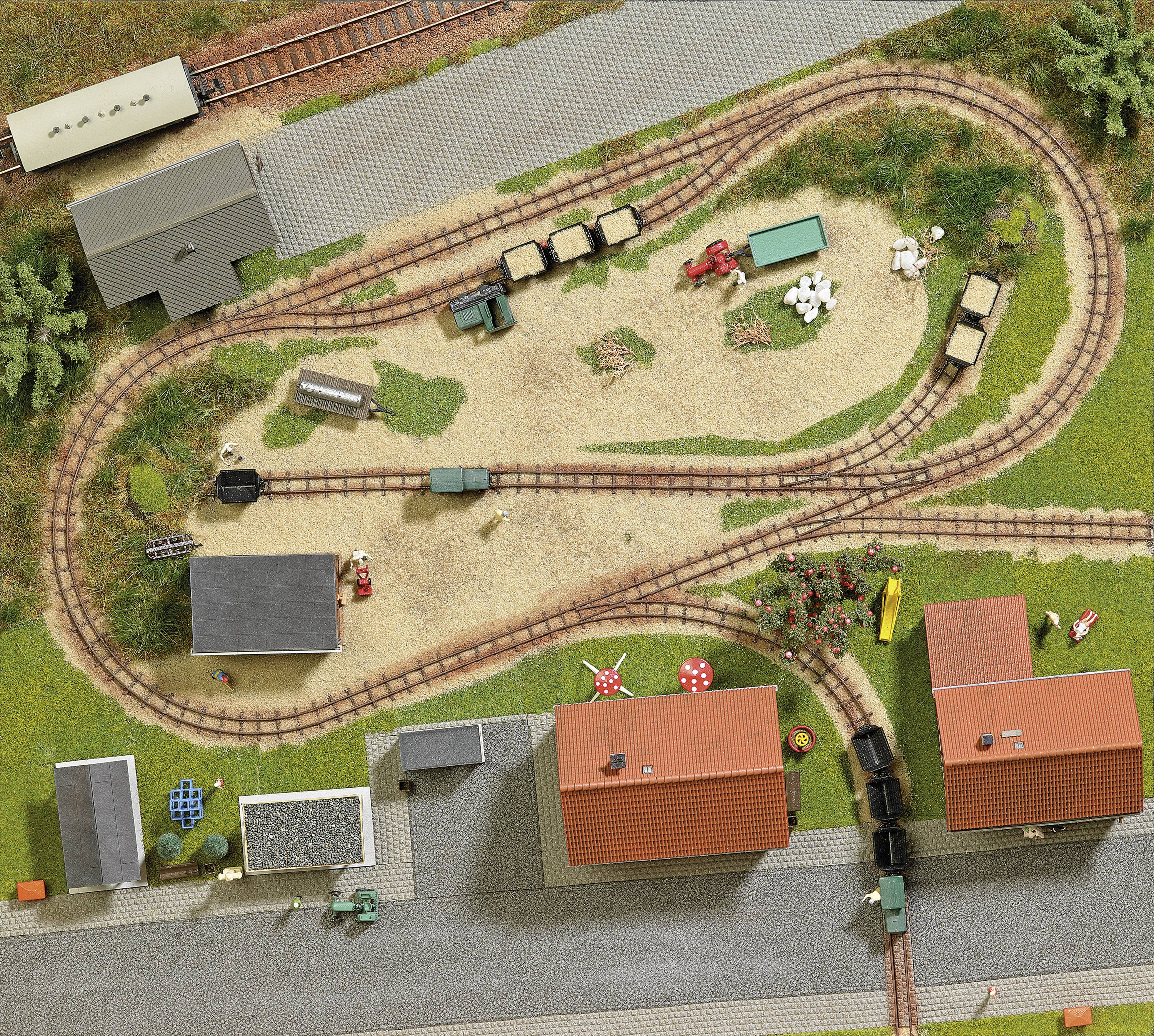 Miniaturmodellbahn aus der Vogelperspektive mit Zügen, Gleisen, Gebäuden und Personen zeigt eine ländliche Szene in einem Dorf.