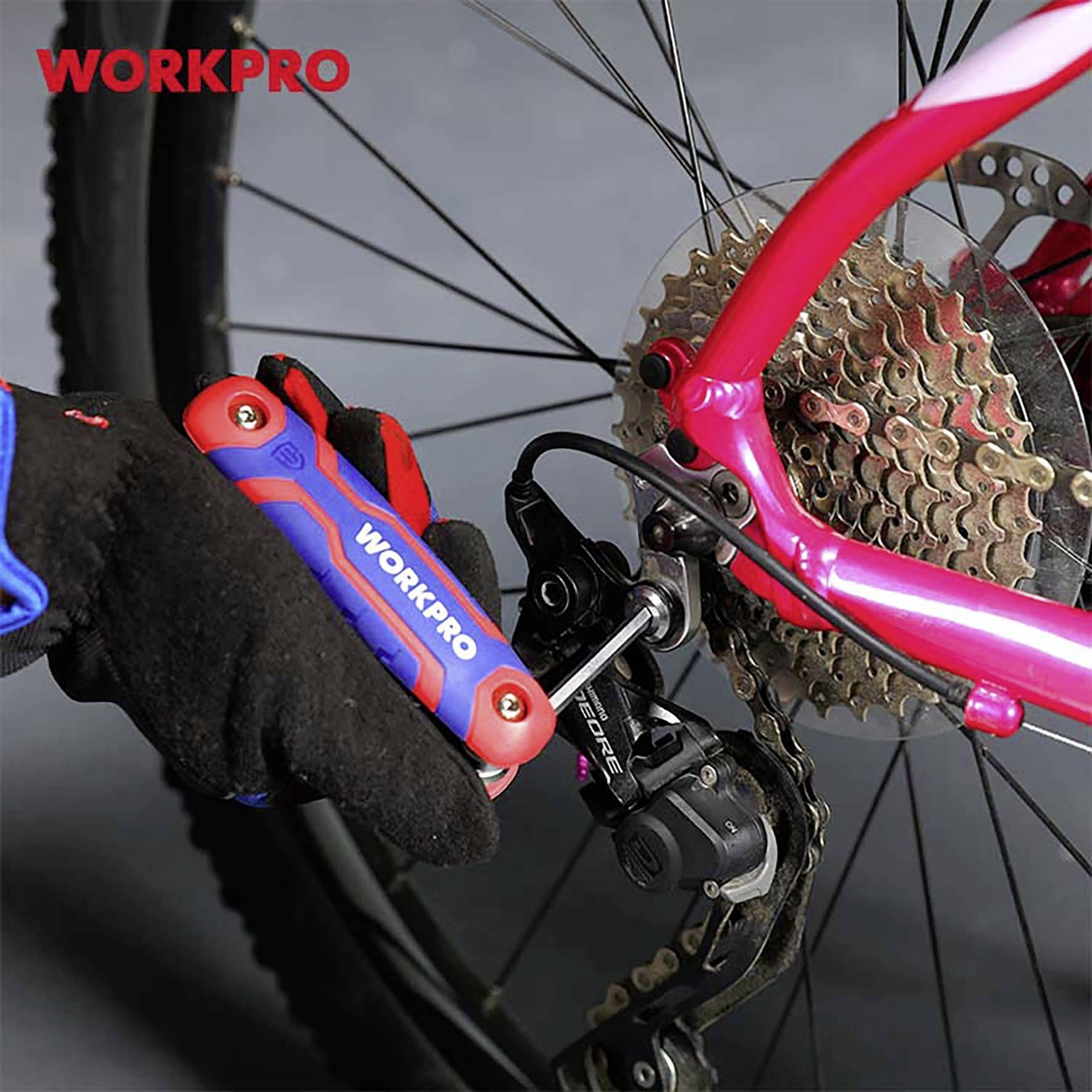 Eine Person verwendet ein WORKPRO-Werkzeug, um das Schaltwerk eines pink-roten Fahrrads zu justieren. Nahaufnahme zeigt die Fahrradkette und Zahnräder.
