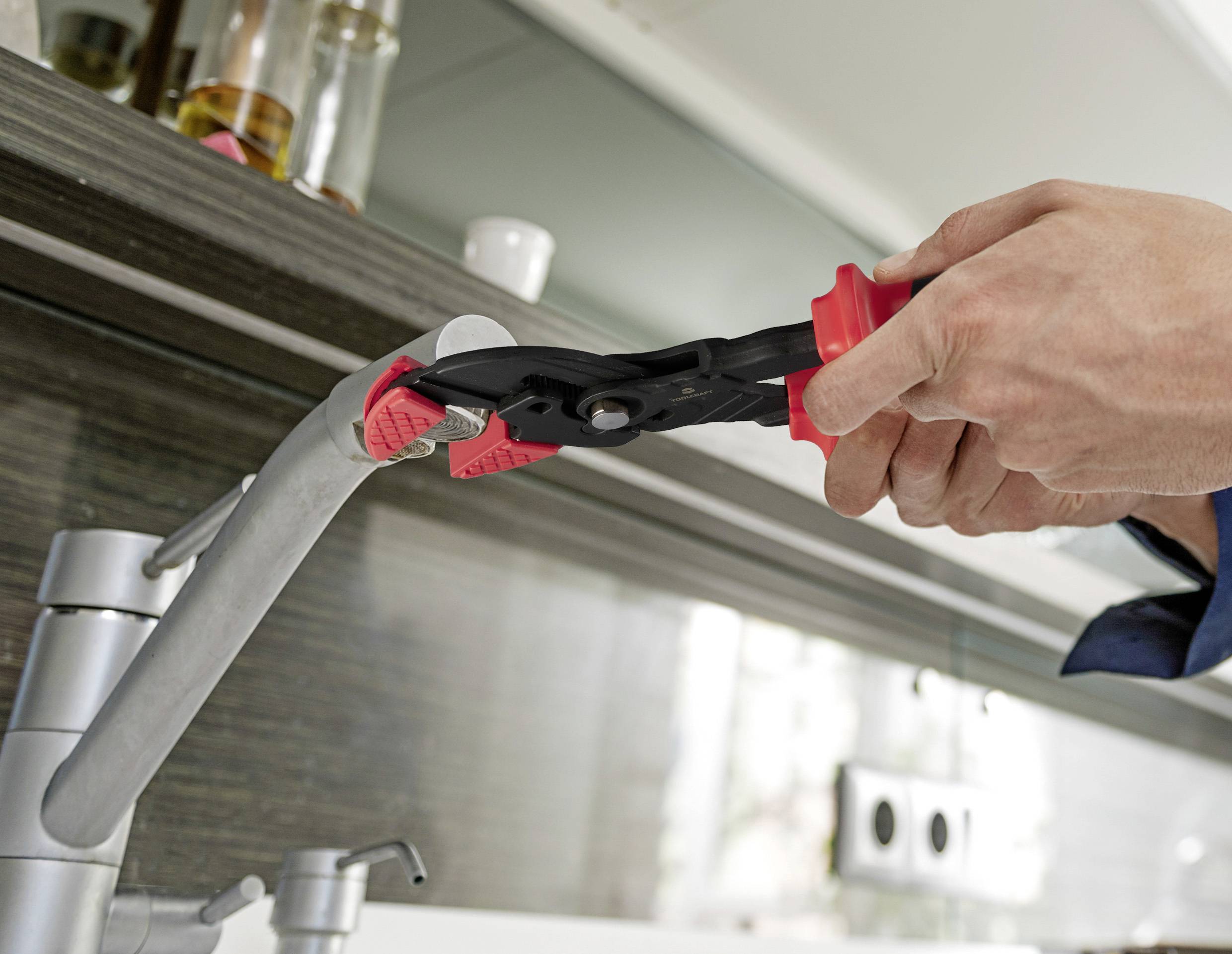 Eine Hand hält eine Rohrzange an einem Wasserhahn in einer modernen Küche, offenbar bei der Installation oder Reparatur.