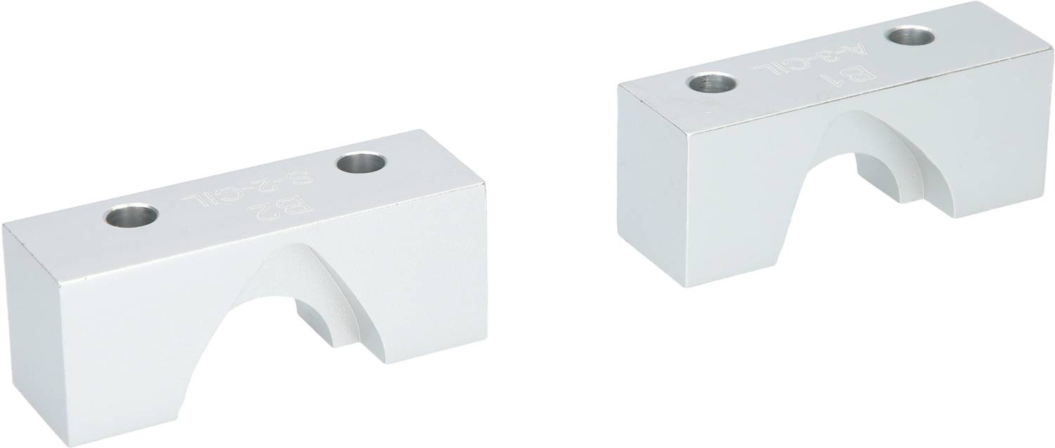 Zwei metallische Halterungsblöcke mit halbrunden Aussparungen und zwei Schraublöchern, vermutlich für die Befestigung von Rohren oder Stangen.