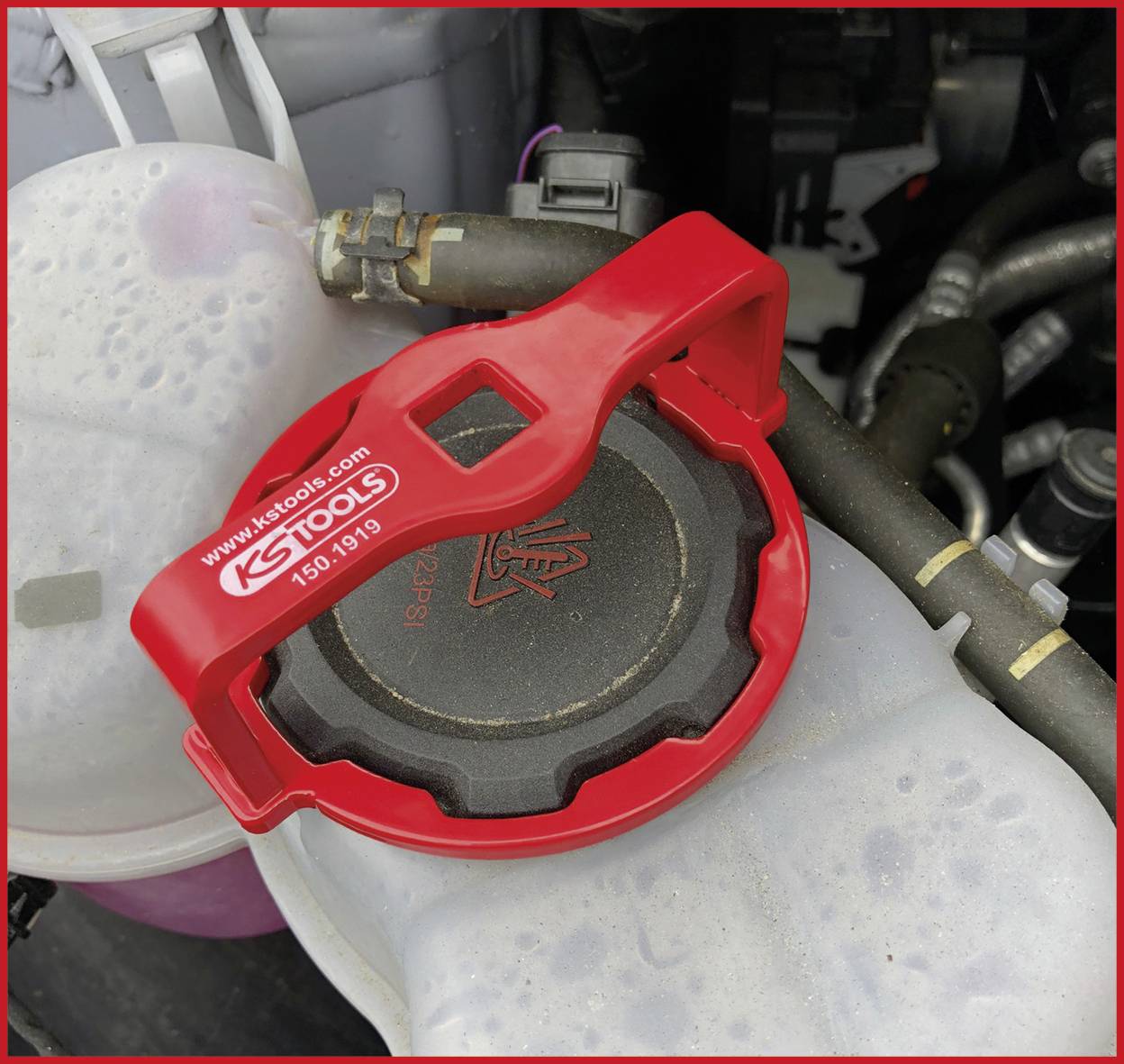 Ein roter Werkzeugsatz von KS Tools liegt auf einem schwarzen Kfz-Teil in einem Motorraum. Etikett mit KS Tools Webadresse sichtbar.