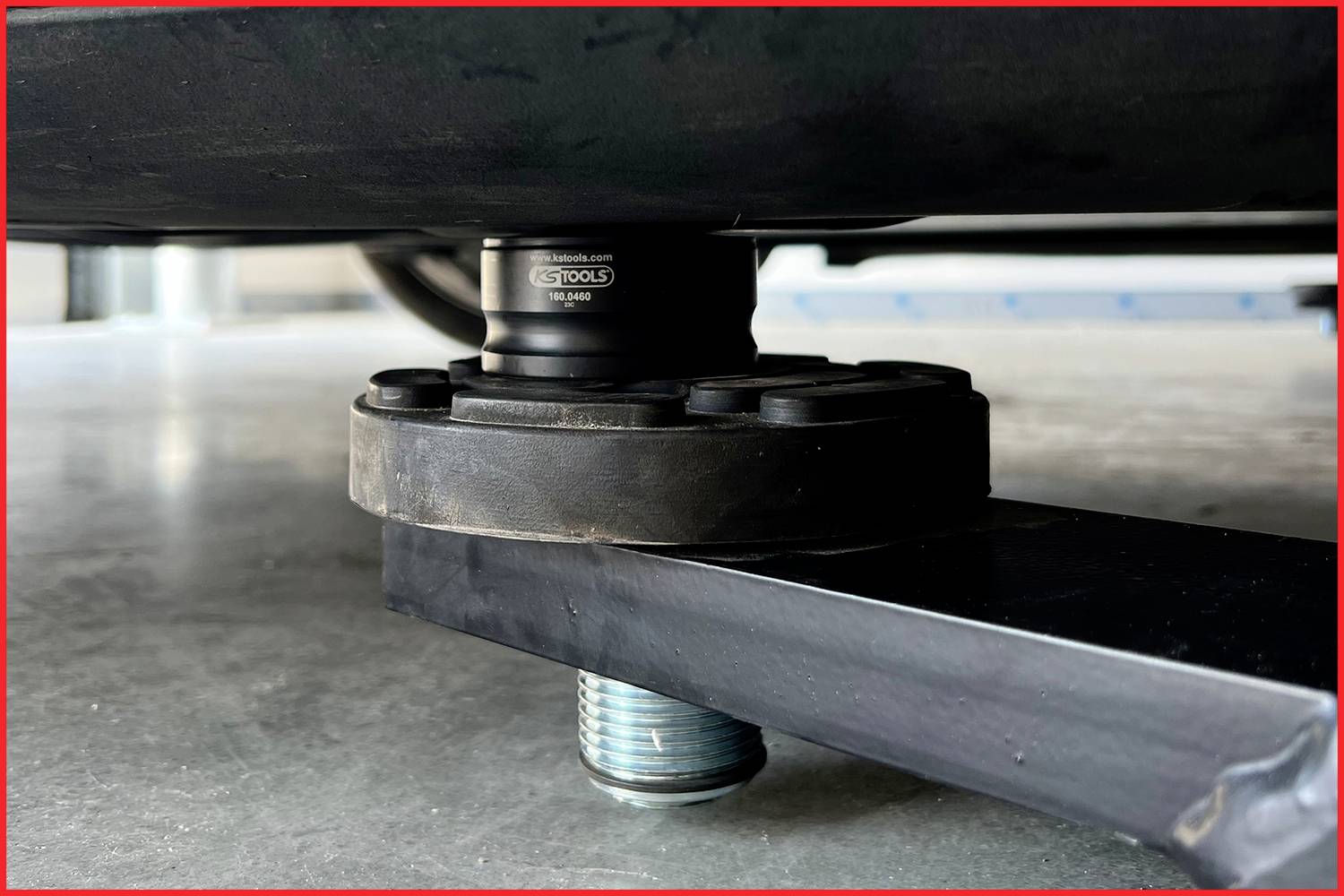 Ein Wagenheber hebt ein Fahrzeug hoch. Man sieht die schwarze Hebeplattform mit Schraubverbindung auf grauem Betonboden.
