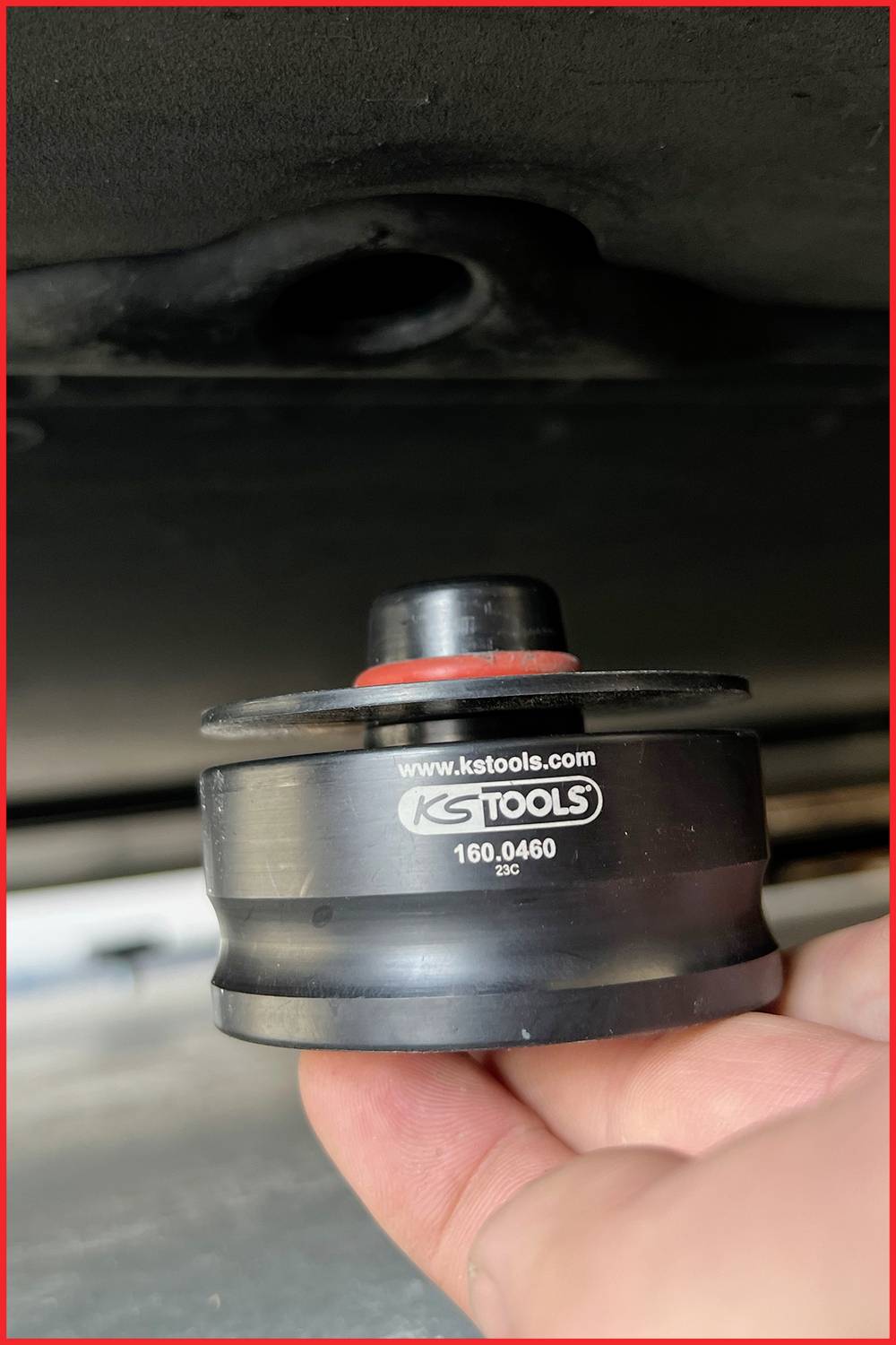 Ein schwarzer Adapter von KS Tools wird von einer Hand gehalten. Aufschrift: 'www.kstools.com 160.0460'. Der Adapter scheint ein Autowerkzeug zu sein.