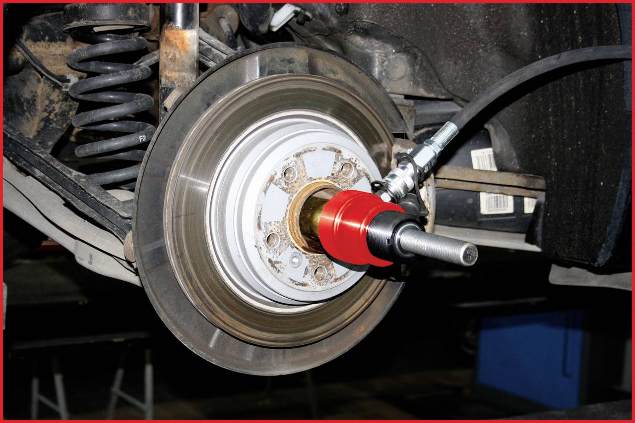 Bremsscheibe eines Autos mit abgenutzten Stellen, montiert an der Fahrzeugachse. Ein Werkzeug ist zum Entfernen bereit.