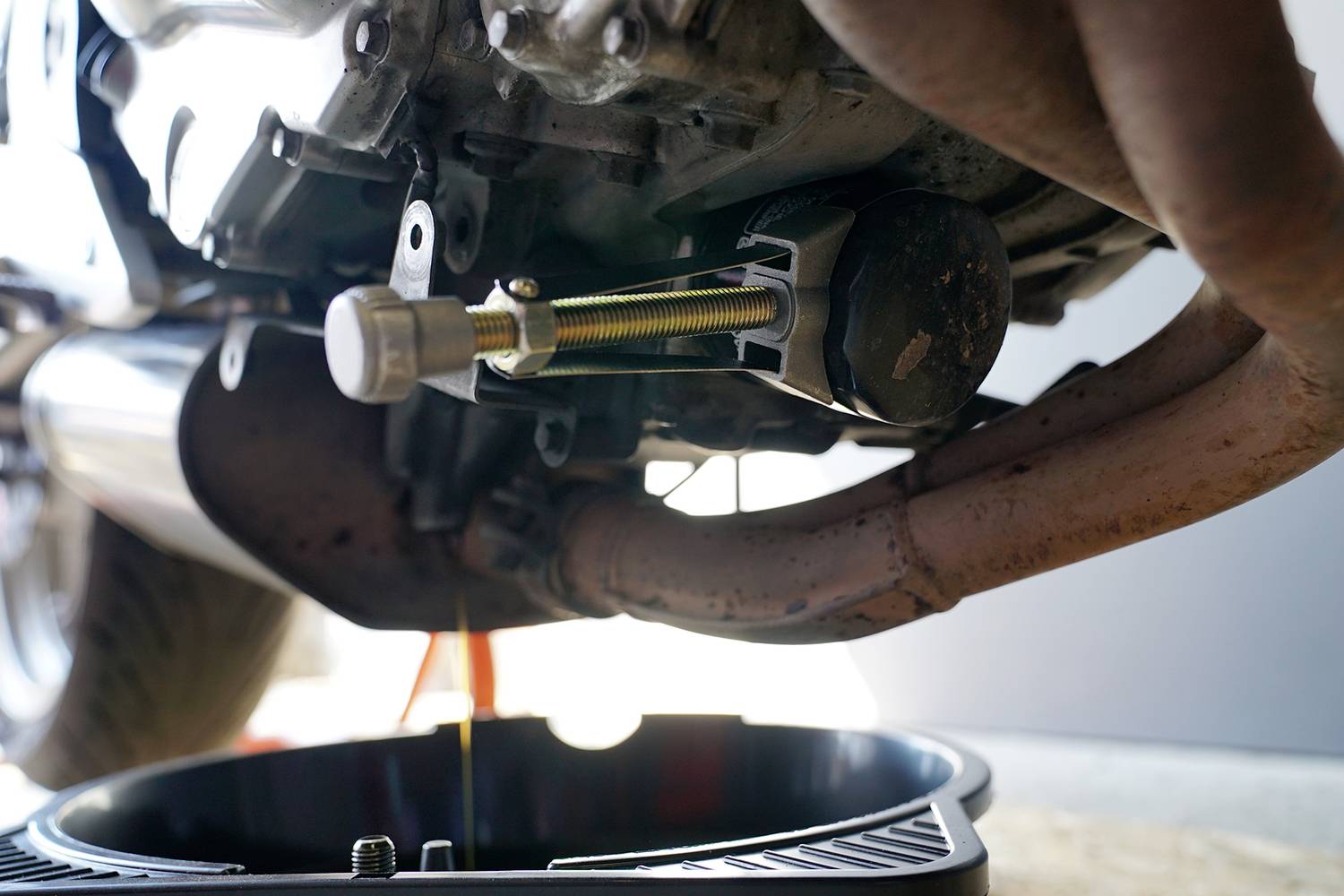 Motorradölwechsel: Ablassen des alten Motoröls in einen Auffangbehälter. Mechanikerwerkzeug für Wartung sichtbar.