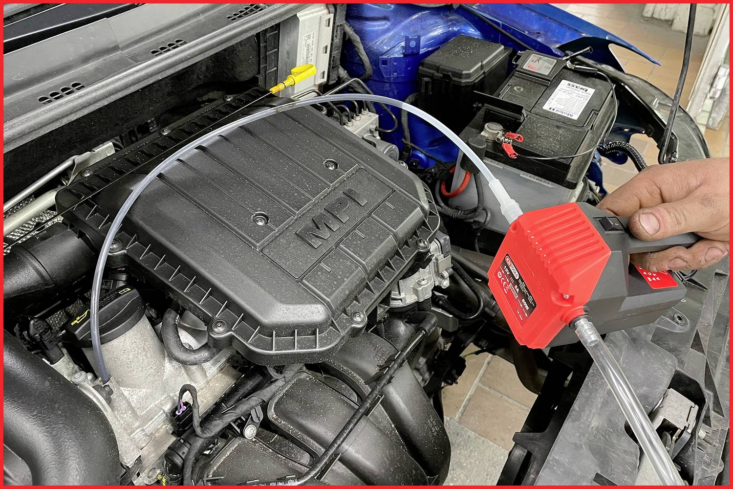 Eine Person prüft den Motor eines Autos mit einem Diagnosegerät. Zu sehen sind der Motorblock und das angeschlossene Gerät.