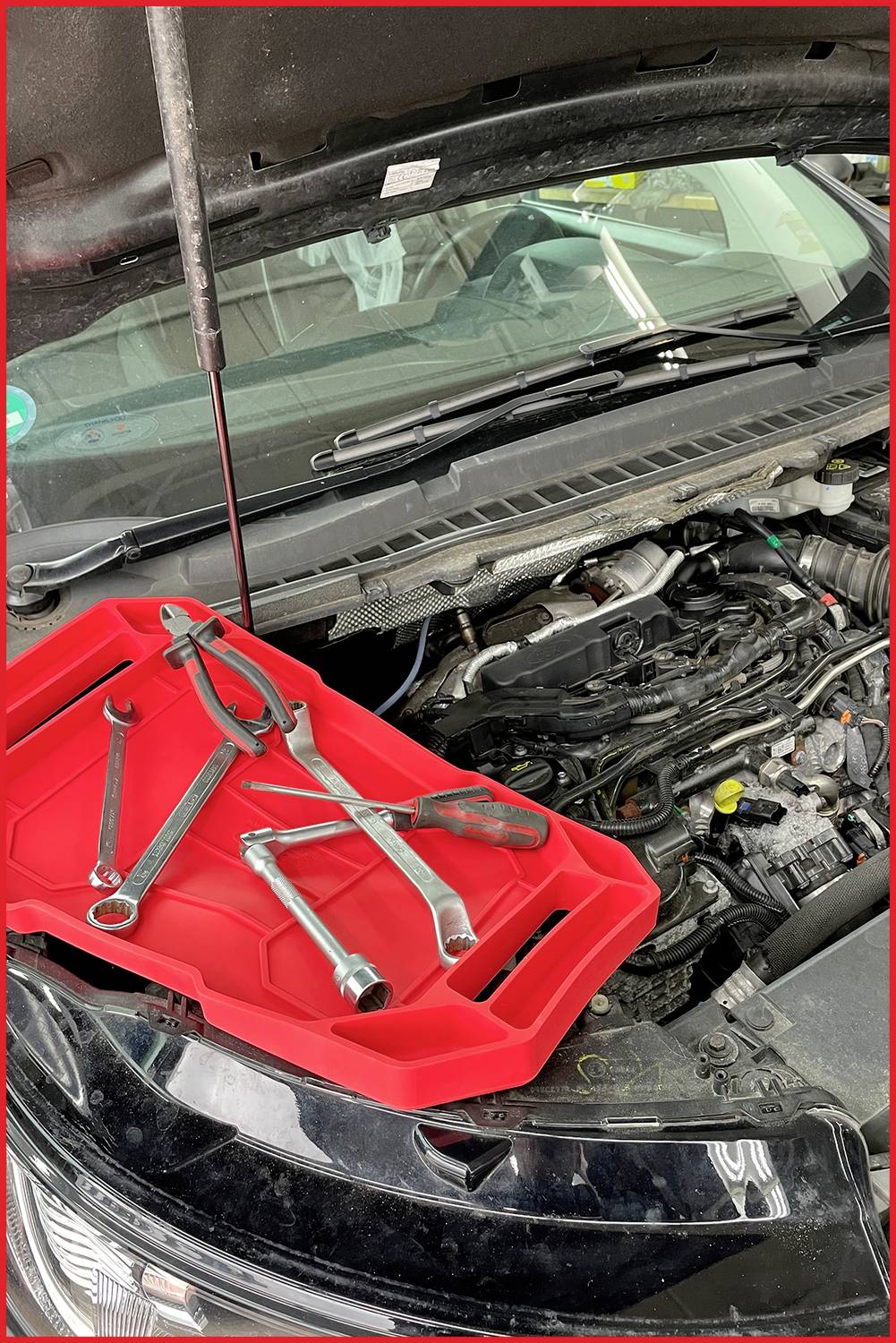 Ein offener Autowagen mit mehreren Werkzeugen auf einer roten Schale über dem Motorraum, bereit für eine Reparatur.