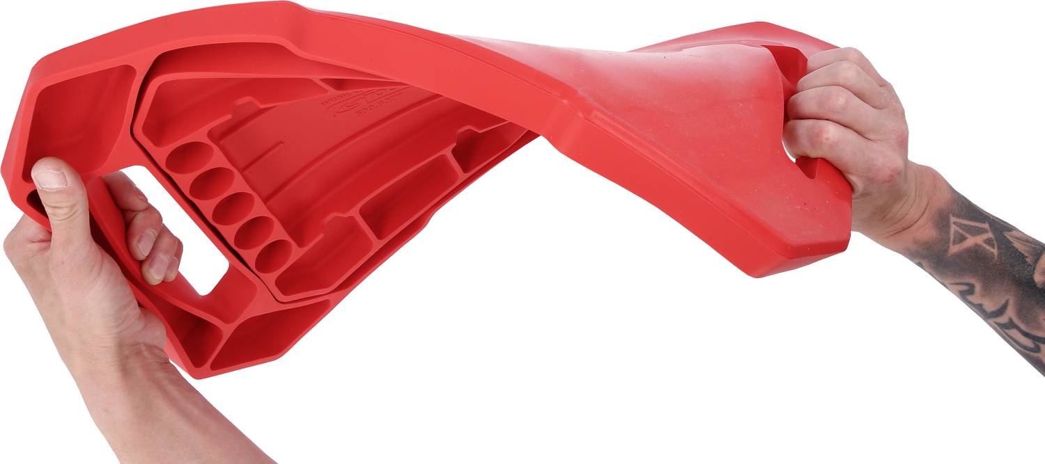 Zwei Hände biegen ein rotes, flexibles Plastikteil mit mehreren Griffen und Löchern. Die rechte Hand hat ein tätowiertes Armgelenk.