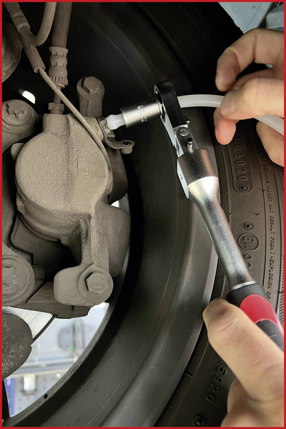 Eine Person verwendet einen Ratschenschlüssel, um eine Autobremsleitung zu befestigen. Die Szene zeigt Details eines Autoreifens und der Bremse.