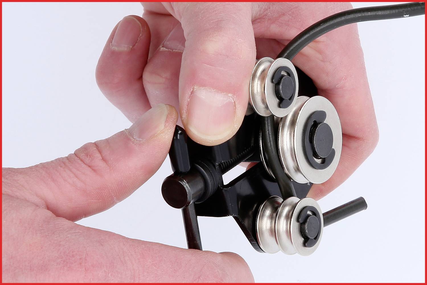 Hände bedienen ein schwarzes Werkzeug mit Rollen, das ein Kabel schneidet oder formt.