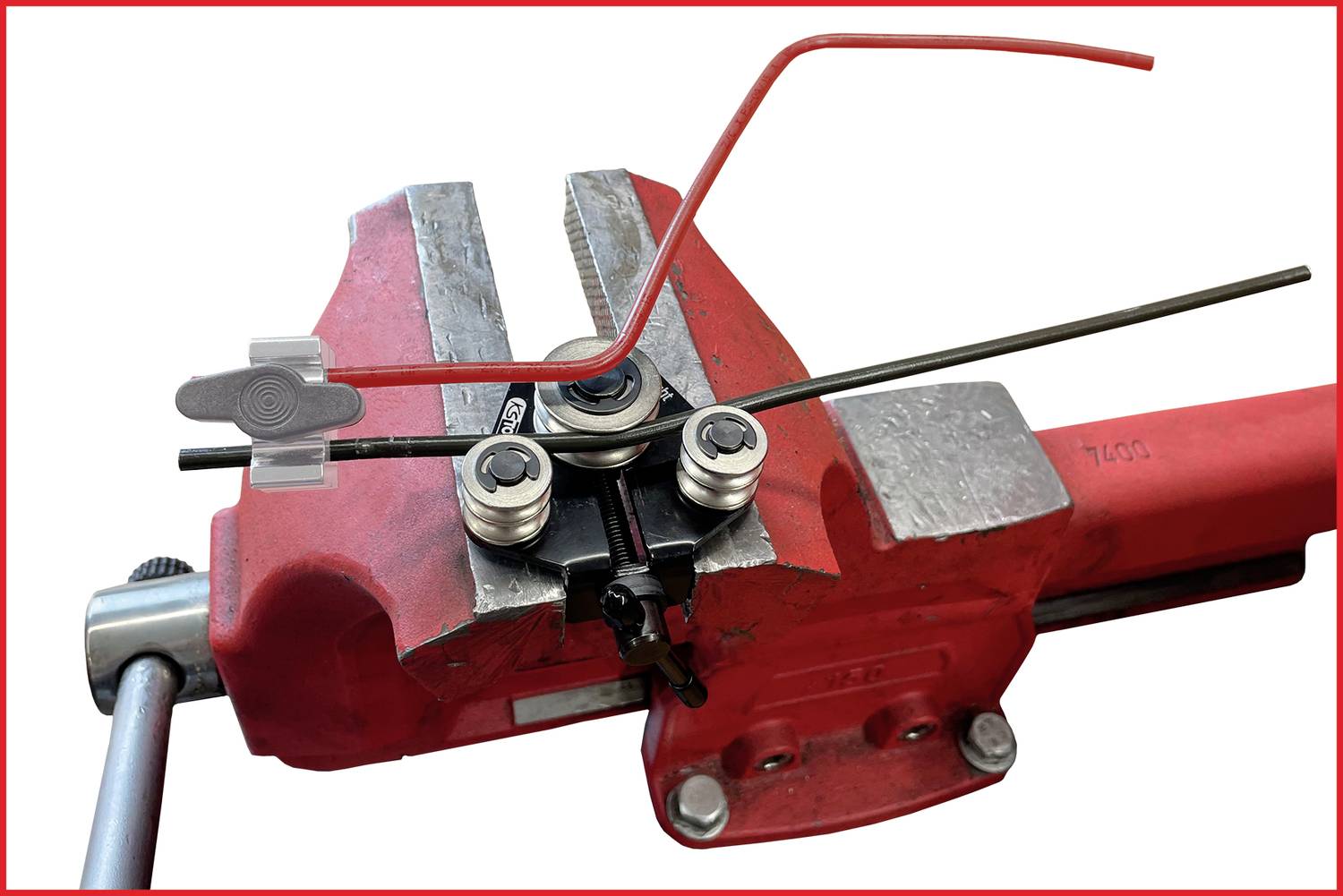 Eine rote Schraubstockklemme hält Metallstangen, die mit Werkzeugen gebogen werden. Ein dünner Draht ist in einer gebogenen Form.