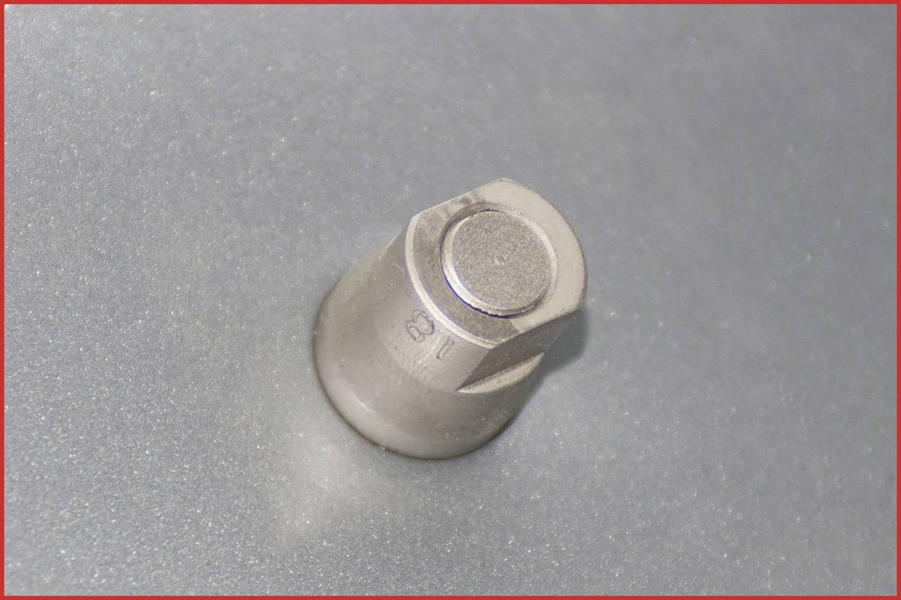 Ein metallischer Stift ragt aus einer glatten Oberfläche heraus.