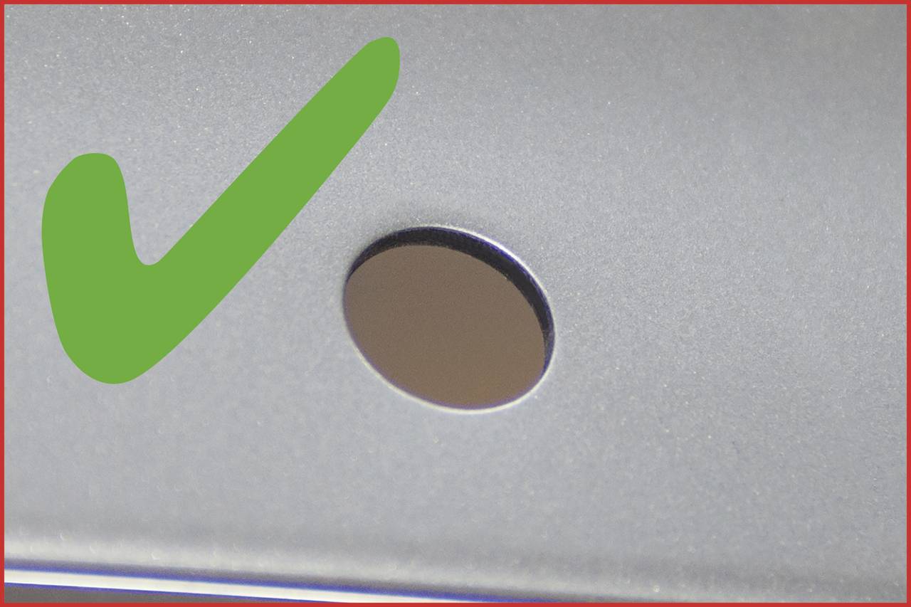 Grüner Haken neben einem runden Loch auf einer metallischen Oberfläche. Symbolisiert Genehmigung oder Korrektheit.