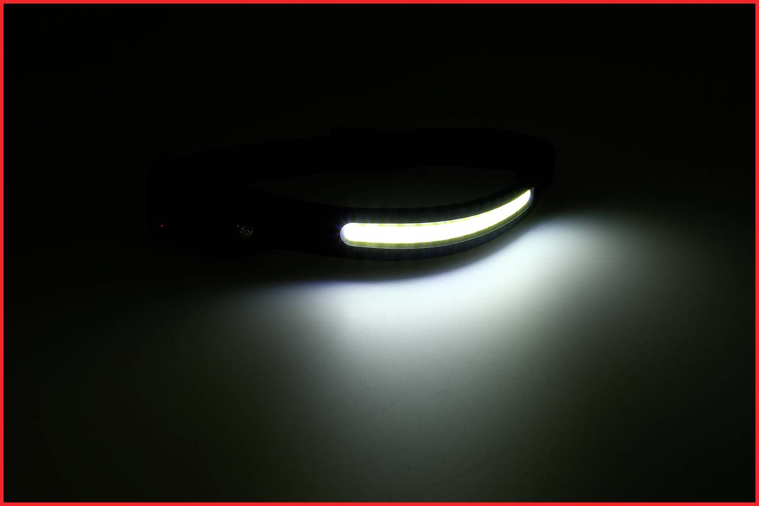 Es ist ein eingeschaltetes Stirnlicht, das auf einer dunklen Oberfläche liegt und einen starken Lichtstrahl abgibt.