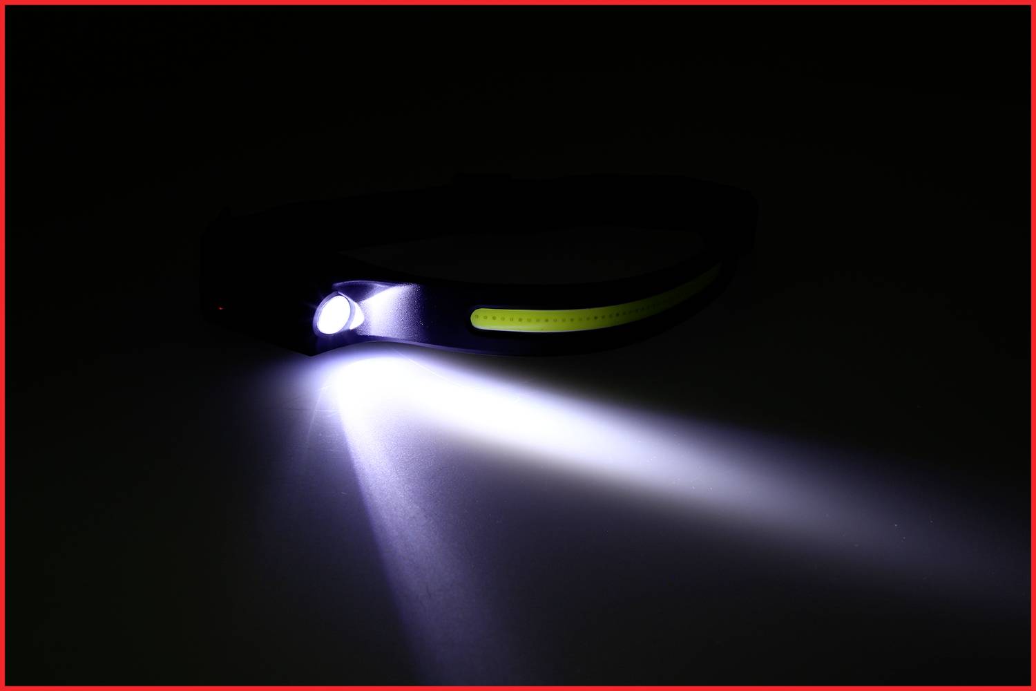 Eine eingeschaltete Stirnlampe liegt auf einem dunklen Hintergrund, wirft einen starken Lichtstrahl nach vorne, Licht ist weiß und hell.