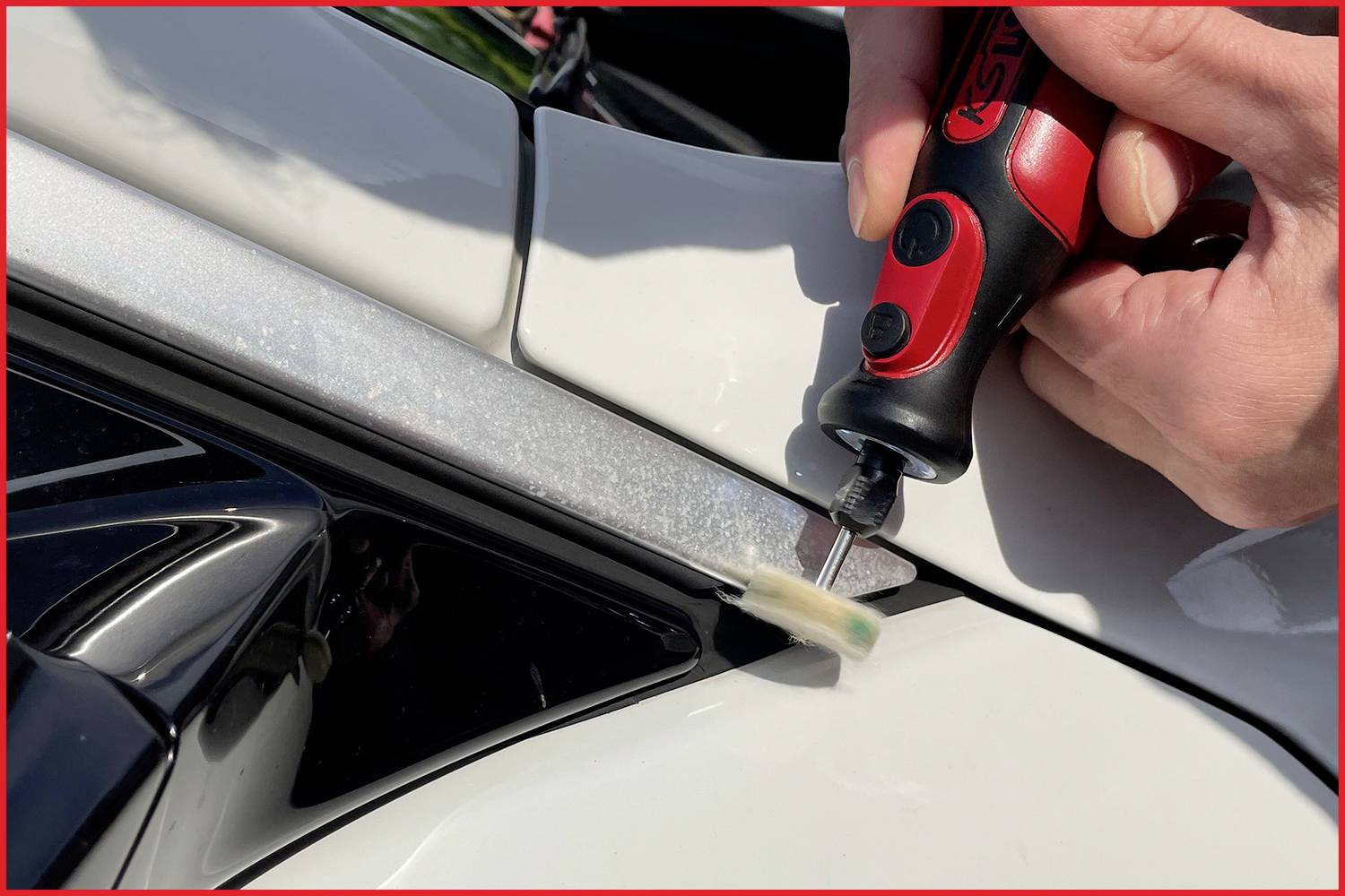 'Nahaufnahme einer Person, die ein kleines Elektrowerkzeug benutzt, um ein Bauteil an einem weißen Auto anzupassen oder zu reparieren.'