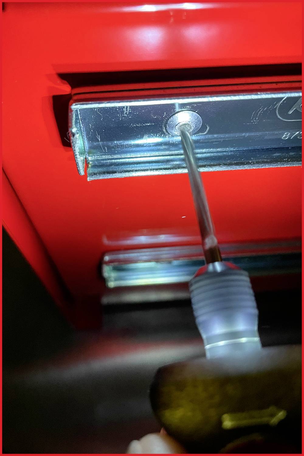 'Nahaufnahme eines Schraubenziehers, der eine Schraube in eine rote Oberfläche dreht.'