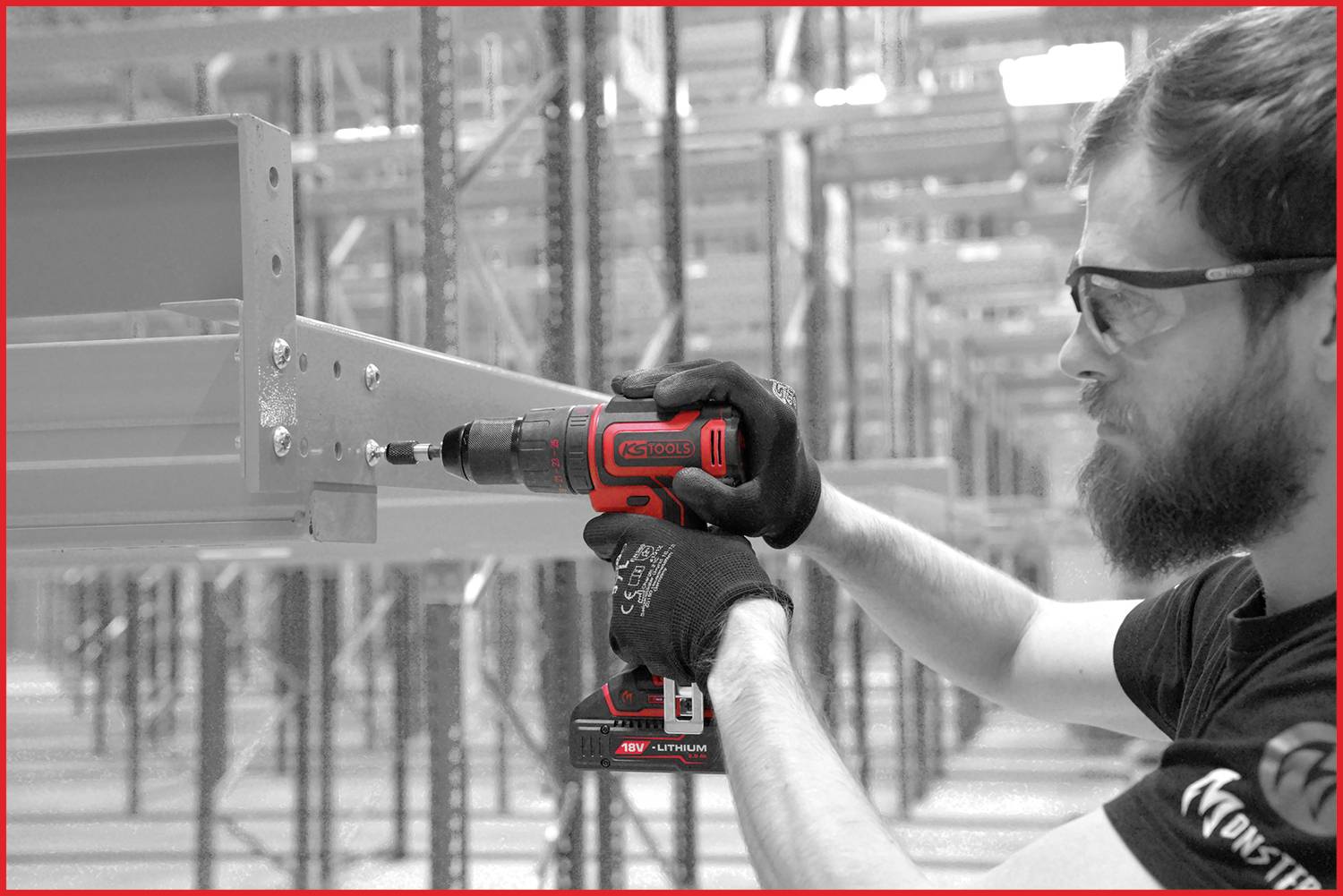 Eine Person montiert ein Regal mit einem Akkubohrer in einem Lager. Schutzbrille und Handschuhe werden getragen, betont Arbeitssicherheit.