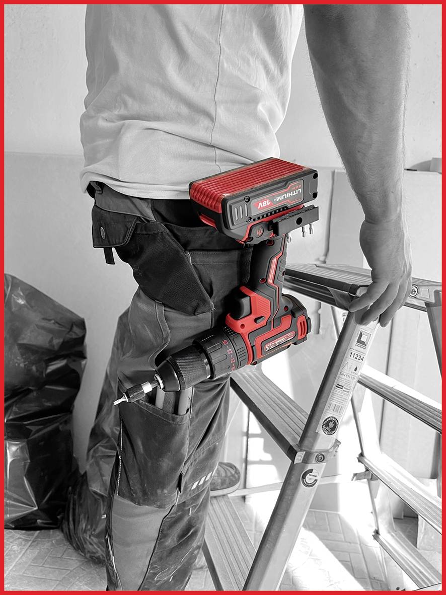 Ein Mann steht auf einer Leiter und hält eine Bohrmaschine. Er trägt Arbeitskleidung. Im Hintergrund sind Werkzeug und Müllsack erkennbar.