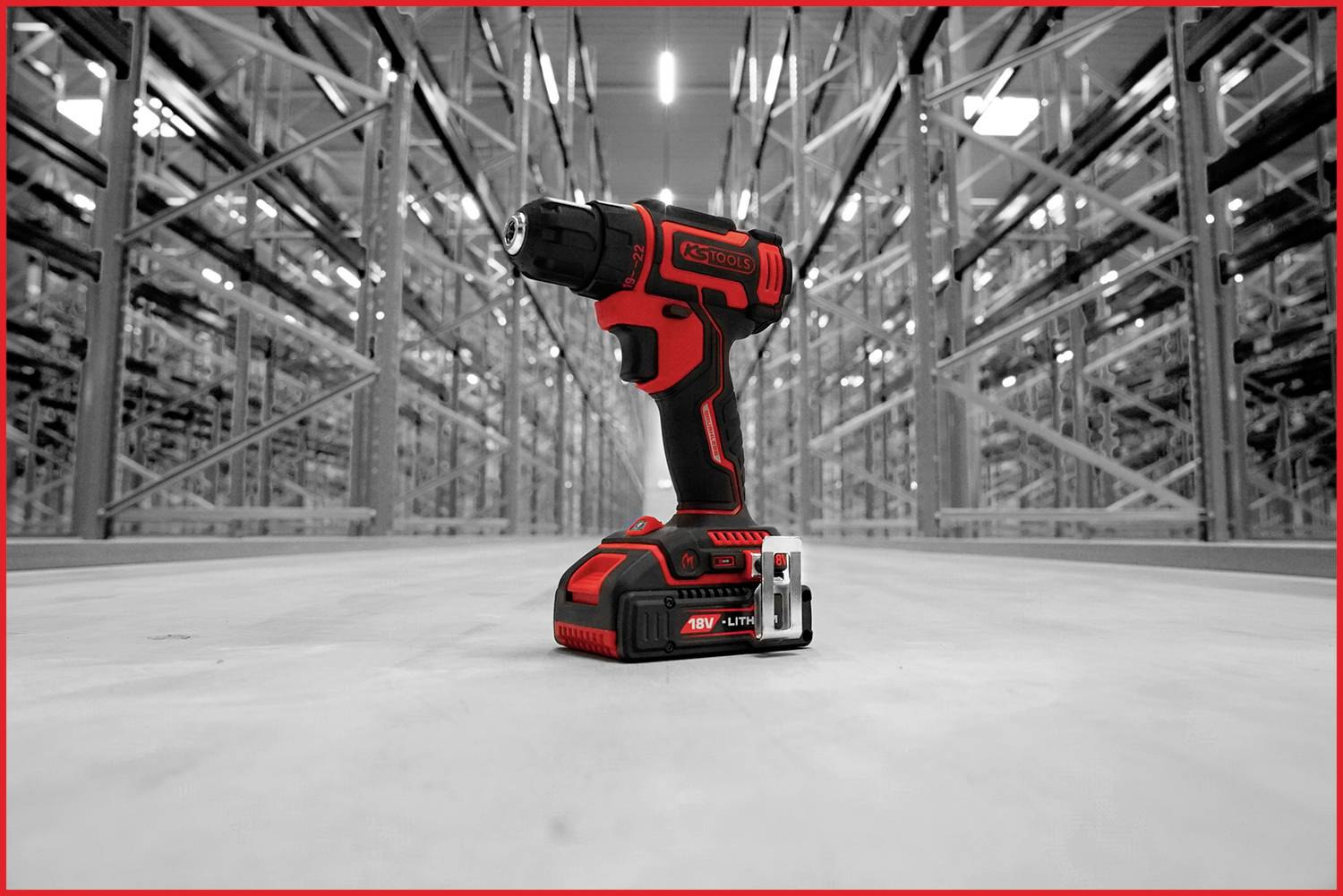Ein roter Akkuschrauber steht auf dem Boden eines großen, gut beleuchteten Lagers. Im Hintergrund sind Regalreihen zu sehen.