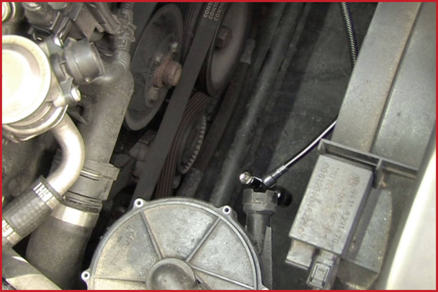 Ein Motorraum mit sichtbaren Teilen wie Riemen, Schläuchen und Metallkomponenten. Im Fokus: der Bereich um die Antriebsriemen.