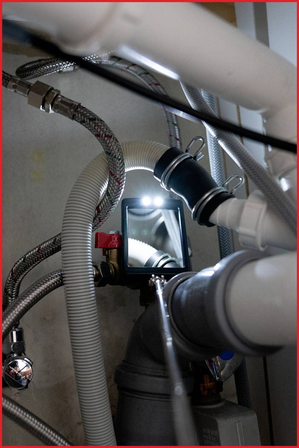 'Eine detaillierte Nahaufnahme von Rohren unter einem Waschbecken. Verschiedene Schläuche und Anschlüsse sind sichtbar.'