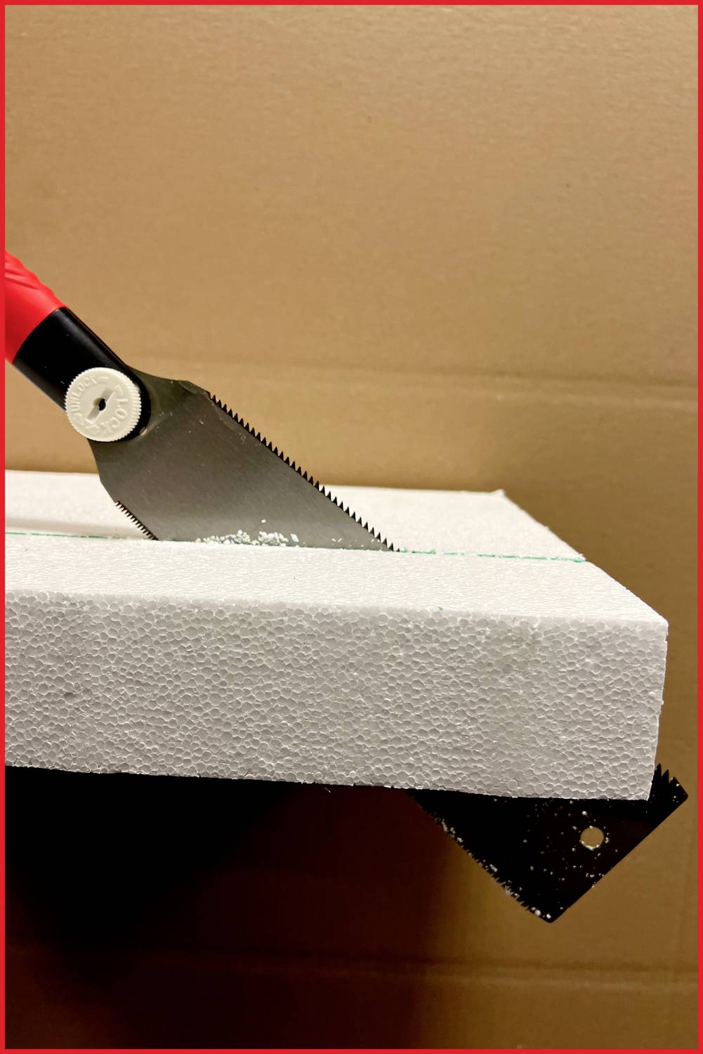 Eine rote Handsäge schneidet durch eine weiße Styroporplatte. Die Szene zeigt eine Präzisionsarbeit in einem handwerklichen Kontext.