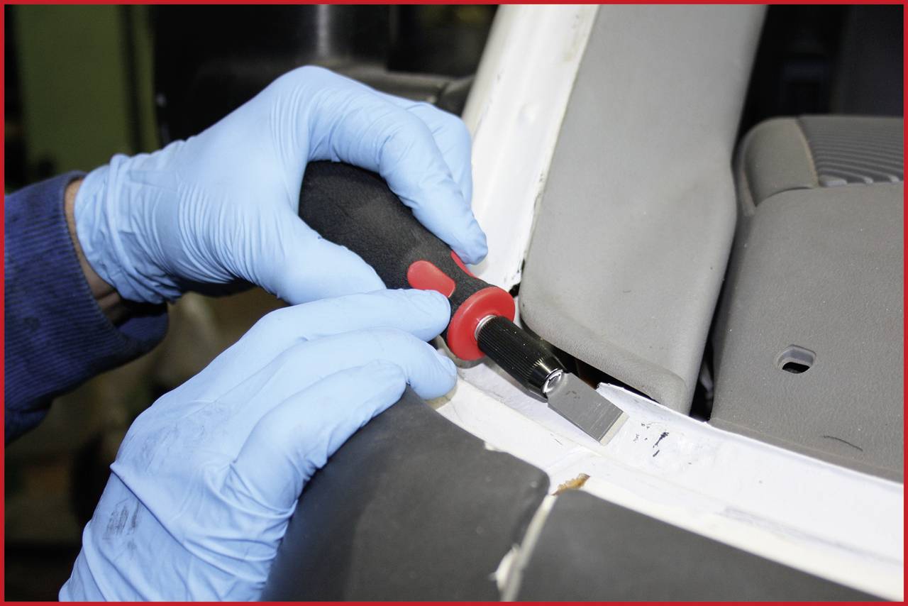 'Eine Person mit blauen Handschuhen repariert ein Autoteil mit einem Werkzeug.'
