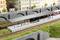 Modelleisenbahn-Szene mit Bahnhof, Zug, Gleisen, und Figuren, die auf den Bahnsteig warten. Hintergrund zeigt Stadthäuser und Brücke.