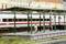 Eine Miniaturmodellbahnszene mit einem überdachten Bahnsteig, auf dem zwei Menschen stehen. Im Hintergrund fährt ein moderner Zug vorbei.