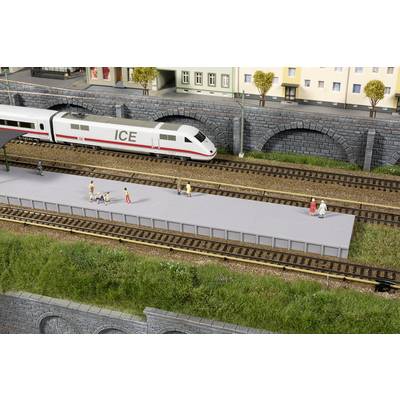 Ein ICE-Zug hält an einem Modellbahnhof mit mehreren Figuren auf dem Bahnsteig. Im Hintergrund sind Gebäude und Brücken zu sehen.